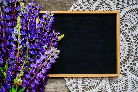 Black chalk board for text on an old wooden table, lupins and vintage crocheted napkin.の写真素材