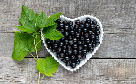 Black currant berries in a white plate in the form of a heart on a wooden background.の写真素材