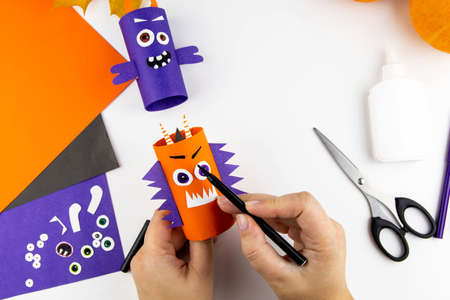 Halloween decoration. DIY and kids creativity concept. Step by step instructions: make a monster from a toilet roll of orange and purple paper. Step 15 draw the eyebrows.の写真素材