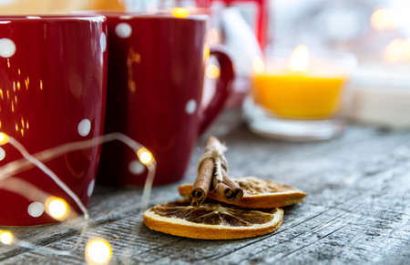 Close-up of dried orange and cinnamon sticks near two red mugs on a wooden background.の写真素材