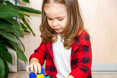 A girl with long hair builds from a plastic construction kit. The girl plays at home.