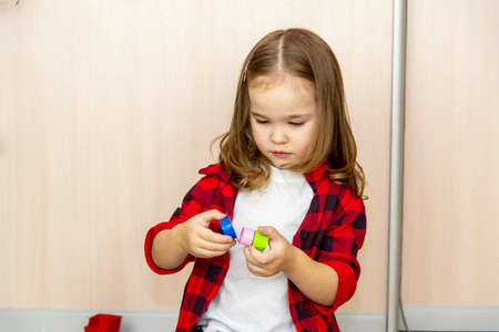 A girl with long hair builds from a plastic construction kit. The girl plays at home.