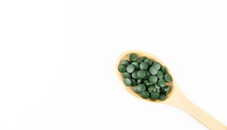 Green spirulina pills in a wooden spoon on a white background. Copy space.の写真素材
