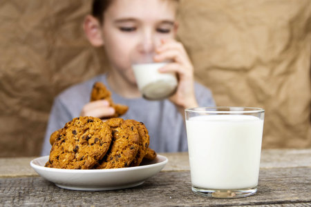 Close-up of cookies and a glass of milk on a wooden table on the background of a boy with milk and cookies.の写真素材