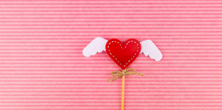 Valentine's Day background. Heart with handmade wings on a pink striped background