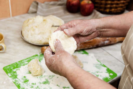 The concept of baking in home conditions. Close-up of the elderly woman's hands knead the doughの写真素材