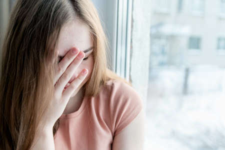 The concept of depression, the sadness of a teenager. The teenage girl covered her face with her handの写真素材