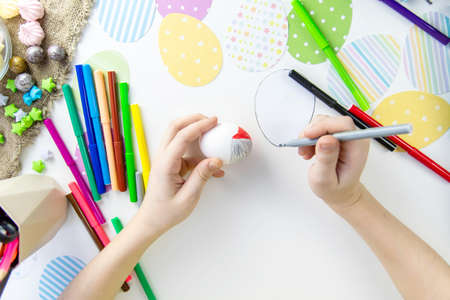 View from above on the white table, children's hands paint the Easter egg with markersの写真素材