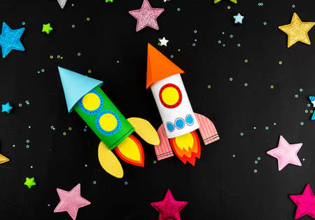Craft space rocket made of colored paper in children's hands.