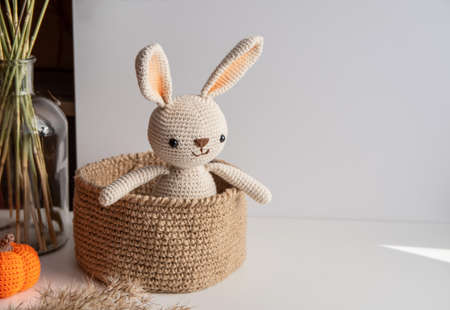 Crocheted bunny sits in a jute basket on a white backgroundの写真素材