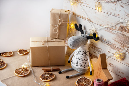 Decor for Christmas in eco style with your own hands. Knitted toy deer, elk, gifts in craft paper, dried oranges, wooden star.の写真素材