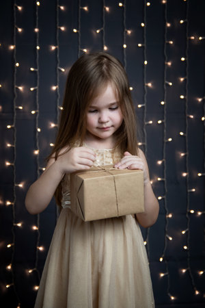 Beautiful little girl in a golden dress wishes a Merry Christmas. Postcard for the New Year. The child smiles and dreams of a miracle. Bokeh in the background.の写真素材