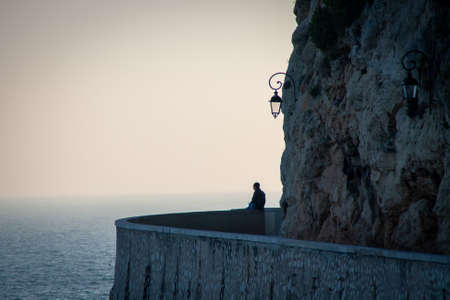 Alone man sit in the sea wall reflectingの写真素材