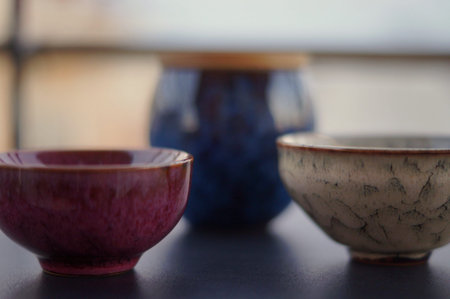 Three handcrafted ceramic vessels in burgundy, blue, and neutral tones are arranged on a dark