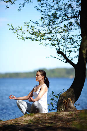 young girl training yoga near a lake under a treeの写真素材