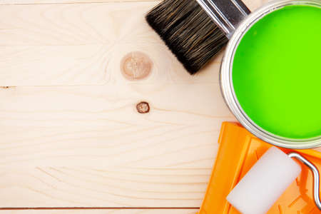 Colorful bucket of green paint on a table. Paintroller in tray with paint can on a wooden background