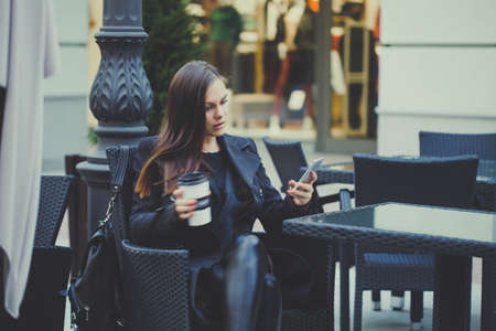Cafe city lifestyle young woman texting message and drinking coffee sitting outdoor in trendy urban cafe.の写真素材