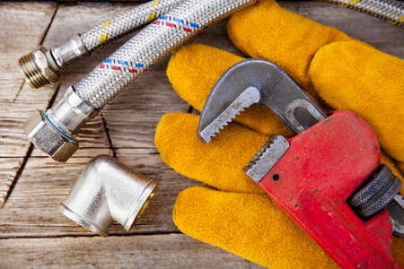 Set of plumbing and tools on the table. Fitting, suede gloves and adjustable wrench for plumbing worksの写真素材