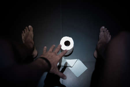 View from above a naked legs man who's sitting on toilet and trying to reach toilet paperの写真素材