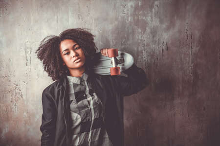 African teenager girl with skateboard in front of a concrete wallの写真素材