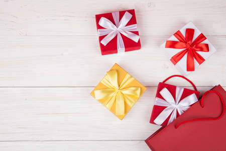 Red paper gift bag with presents boxes on white wooden background. Copy spase for your textの写真素材