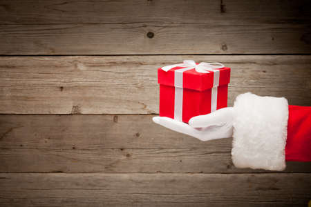 Santa hand holding a red gift box against wooden backgroundの写真素材