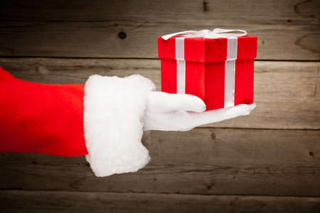 Santa hand holding a red gift box against wooden backgroundの写真素材