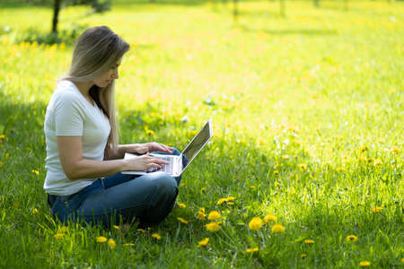 Young woman with laptop sitting on green grassの写真素材