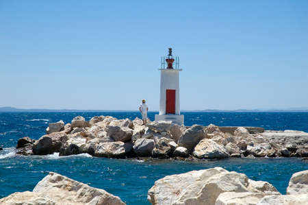 A man standing next to a small light house on a windy dayの写真素材