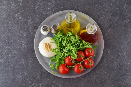 Ingredients for the traditional Italian caprese salad on a glass trey on a grey background with bottles of olive oil and wine vinegar.の写真素材