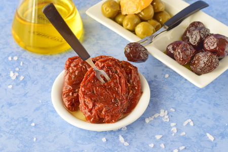 A set of dishes of greek cousine: olives, sun dried tomatoes, lemon, glass jar with olive oil. Traditional Greek food. Mediterranean lifestyle.の写真素材