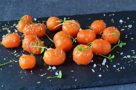 Honey glazed baby carrots with sea salt and thyme in a metal bowl on a grey abstract background....