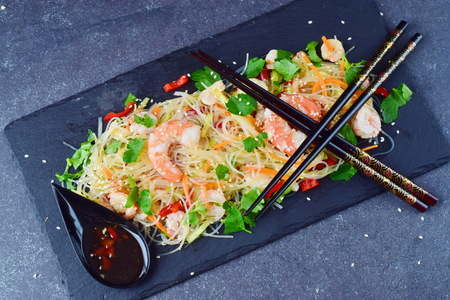 Noodles with prawns and vegetables on a black stone plate with traditional oriental sauce on a grey abstract background. Healthy food conceptの写真素材