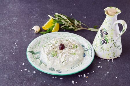 Homemade Greek traditional sauce tzatziki in a traditional colored bowl and a traditional jar with olive oil on a dark abstract background. Healthy eating concept. Mediterranean lifestyleの写真素材