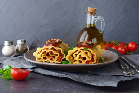 Pasta rolls with vegetables: paprika, onion, olives, mushrooms, tomato, glass jar with olive oil on a light brown plate on a grey abstract background. Vegetarian food. Dieting. Mediterranean lifestyleの写真素材