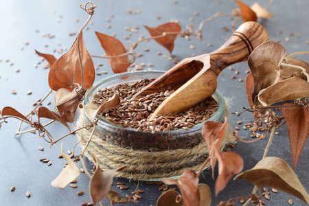 A glass bowl of flax seeds with olive scoop surrounded by artificial flowers on a grey abstract background. Healthy eating concept. Romantic imageの写真素材
