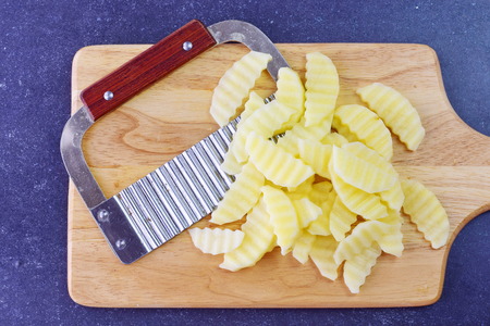Potato peeled and cut in pieces with a special knife with ribs on a cutting board on a grey background. Cooking step by step. Home cooking, Healthy eating conceptの写真素材