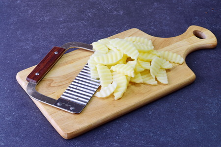 Potato peeled and cut in pieces with a special knife with ribs on a cutting board on a grey background. Cooking step by step. Home cooking, Healthy eating conceptの写真素材