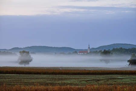 Sunrise in rural Hungary on a misty morning. Tolna hills and the church of Regolyの写真素材