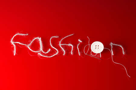 'Fashion' inscription design made of a thread, with a needle and a button on a red gradientの写真素材