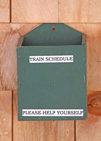 An empty train schedule holder screwed to cedar shingle siding. 
