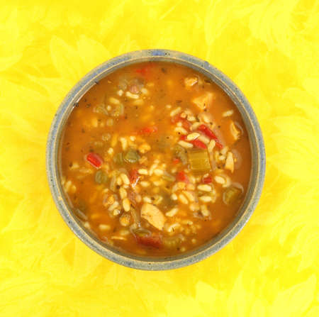 A serving of spicy chicken soup in a stoneware bowl on a yellow floral cloth. の写真素材