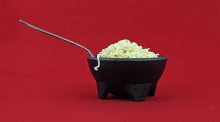 A serving of noodles in a black bowl against a red background.の写真素材