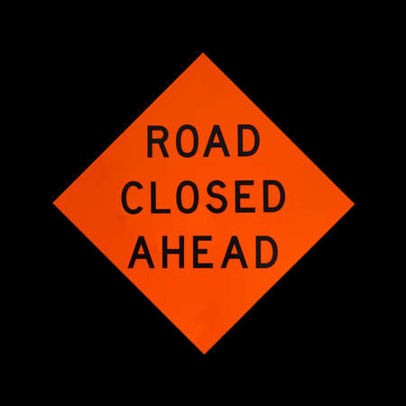 A bright orange warning sign stating the road is closed ahead on a black background.の写真素材