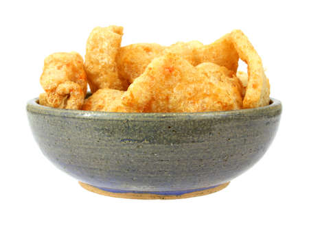 An old stoneware bowl filled with barbecue seasoned pork rinds in on a white background.の写真素材