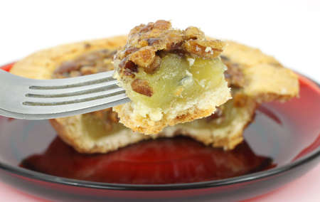 A small bite of pecan pie on a fork with the remainder of the pie in the background on a red dish.の写真素材