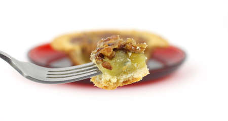 A small pecan pie on a small red dish in the background with a fork filled with one bite in the foreground.の写真素材