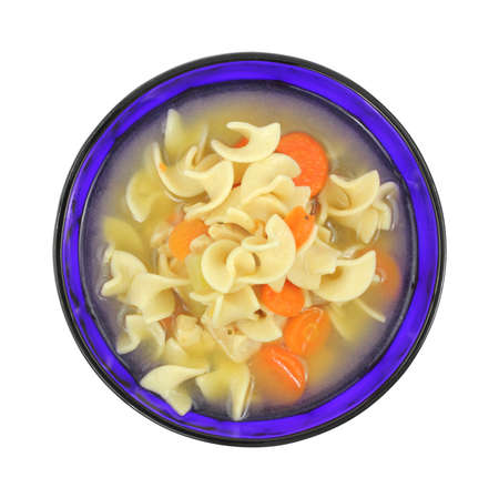 A serving of chicken soup with pasta and carrots in a colorful blue bowl on a white background.の写真素材