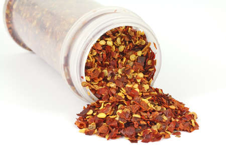 A jar filled with crushed red pepper seasonings spilling onto a white background.