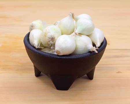 A black bowl filled with white boiling onions on a wood cutting board.の写真素材